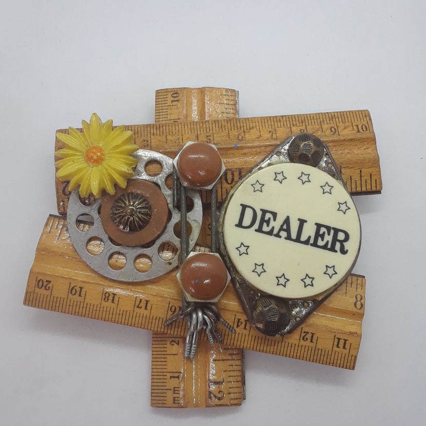Assemblage art featuring various found objects, including pieces of a ruler, a dealer chip and other small odds and ends.
